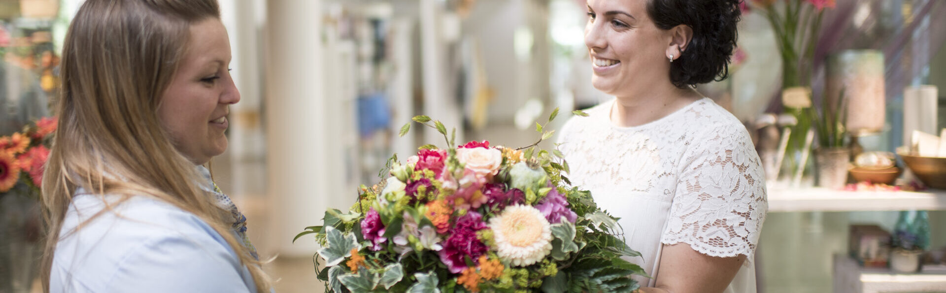 Mitarbeiterin übergibt Kundin einen Blumenstrauss